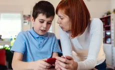 Smiling boy using smartphone with his mother at home